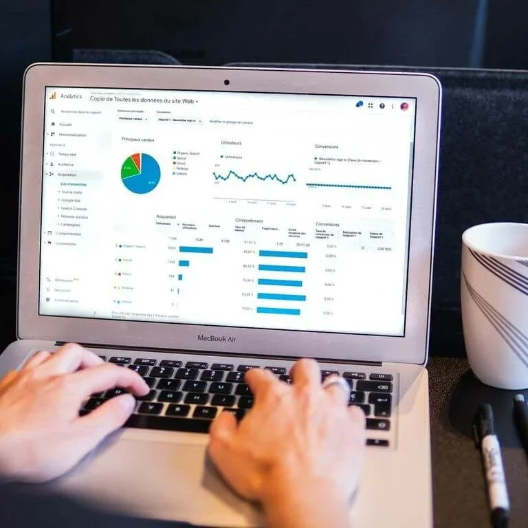 Person arbeitet am Laptop mit Diagrammen und Statistiken, Kaffeetasse daneben.